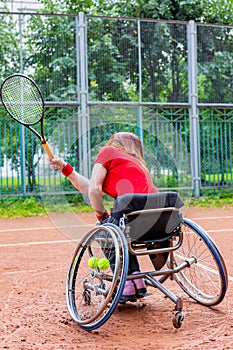 Disabled young woman on wheelchair playing tennis on tennis court.