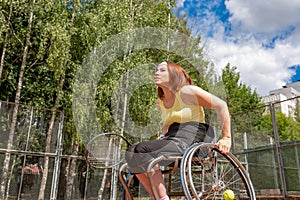 Disabled young woman on wheelchair playing tennis on tennis court.