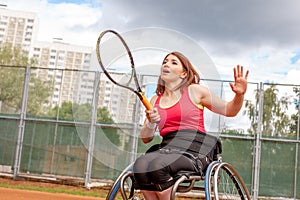 Disabled young woman on wheelchair playing tennis on tennis court.