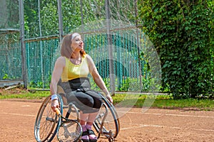 Disabled young woman on wheelchair playing tennis on tennis court.