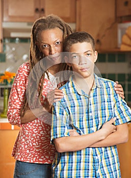 Disagreeable teen boy stands grimacing beside his loving mother