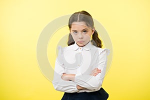 Disagreement and stubbornness. Girl school uniform serious face offended yellow background. Kid unhappy looks strictly