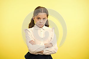 Disagreement and stubbornness. Girl school uniform serious face offended yellow background. Kid unhappy looks strictly