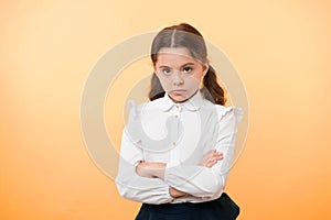 Disagreement and stubbornness. Girl school uniform serious face offended yellow background. Kid unhappy looks strictly photo
