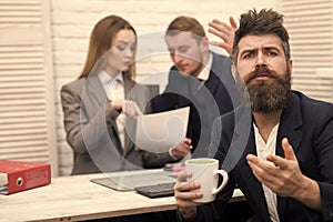 Disagreements in business. Man with beard on hopeful face holds mug, bosses, coworkers, colleagues on background