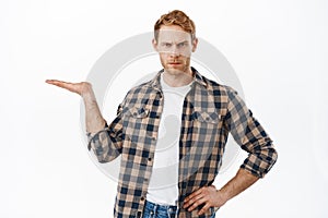 Disappointed adult man with red hair, holding an object in open hand, looking judgemental, showing an item in his palm photo