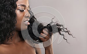 Disappointed african american woman looking at her dry damaged hair