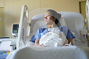 Disappointed Asian chinese woman patient lying in hospital ward and looking out of the window