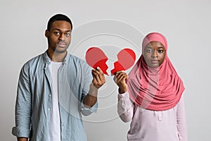 Disappointed black man and woman holding halves of broken heart