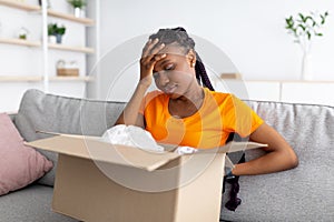Disappointed black woman unboxing her delivery, looking inside wrong box, touching her forehead in frustration