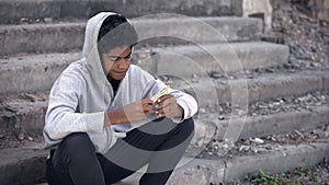 Disappointed black young man thinking of money sitting alone stairs, poverty