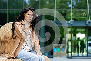Disappointed business lady sitting on bench outside building and experiencing throat pain. Frustrated caucasian female