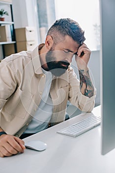 Disappointed businessman sitting at computer desk and leaning head on hand