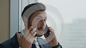 Disappointed businessman talking phone emotionally standing in office close up.