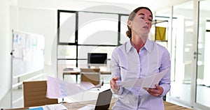 Disappointed businesswoman sitting at desk throws papers