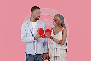 Disappointed couple holding two pieces of broken red paper heart
