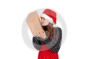 Disappointed girl in christmas hat holding a big gift in her hand. isolated on white background. holidays concept