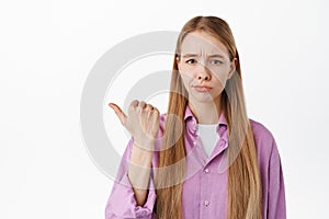 Disappointed girl look skeptical, pointing finger left at something lame, bad and uninteresting product, standing
