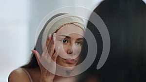 Disappointed girl looking mirror in bathroom. Worried lady checking wrinkles