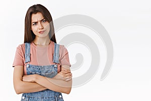 Disappointed, hesitant and skeptical serious-looking young bossy woman in dungarees over t-shirt, cross hands chest