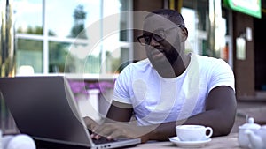 Disappointed man checking email on laptop pc in outdoor cafe, receiving bad news