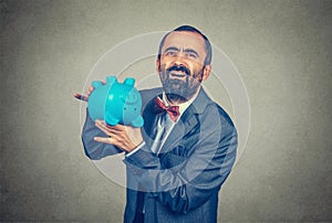 Disappointed man holding overturned piggy bank, showing its emptiness