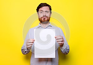 Disappointed man holding white cardboard on yellow background