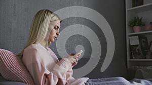 Disappointed sad young woman typing text message while sitting on sofa at home