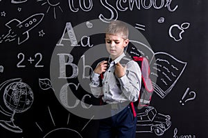 Disappointed schoolboy standing before the chalkboard as a background with a backpack on his back. Landscape picture