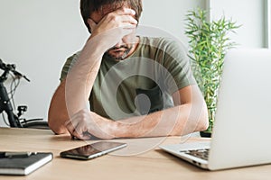 Disappointed telecommuter at home office desk covering face with his hand photo