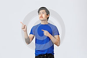Disappointed and upset cute asian guy, man in blue t-shirt sobbing and looking at promo with jealousy or regret