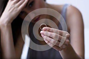 Disappointed wife depressed after divorce, holding a wedding ring sitting on a white sofa