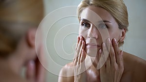 Disappointed woman looking at face reflection in mirror, anti-aging injections