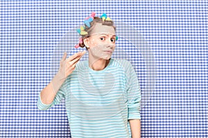 Disappointed woman with skincare product on face, with hair curlers