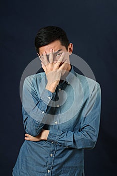 Disappointed young Asian man covering his face by palm