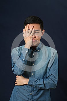 Disappointed young Asian man covering his face by palm