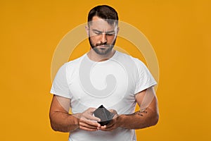Disappointing sad middle aged european male look at empty wallet, isolated on yellow background