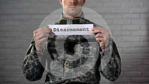 Disarmament word written on sign in hands of male soldier, end of war, peace