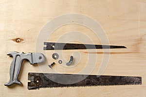 A disassemble hand saw lying on a sheet of plywood