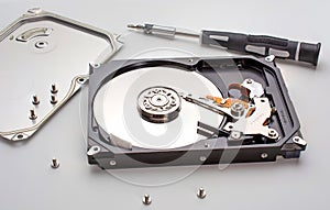 Disassembled computer hard disk inside view with a mirrored disk, on which data is written, and a magnetic head. screwdriver and