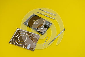 Disassembled hard drive with screwdrivers on a yellow background