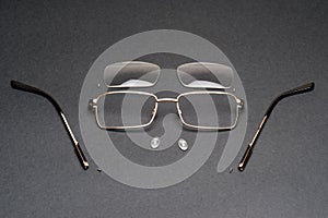 Disassembled metal frame eyeglasses on black surface,lens