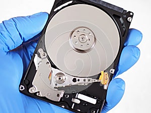 Disassembled open computer PC hard drive HDD close-up. The device holds a hand in a blue rubber glove. White background, not