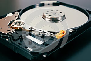 A disassembled open hard disk drive HDD of a computer or laptop close-up.  Device lies on a dark matte surface. Tinted