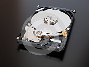 A disassembled open hard disk drive HDD of a computer or laptop lies on a dark matte surface. Close-up. IT&C. Illustration: