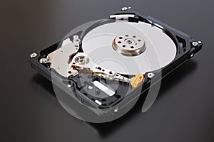 A disassembled open hard disk drive HDD of a computer or laptop lies on a dark matte surface. Close-up. IT&C. Illustration: