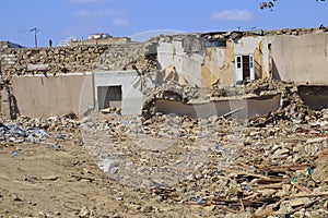 Disaster scene full of debris, dust and damaged house.