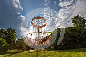 Disc golf basket and flying disc in summer park