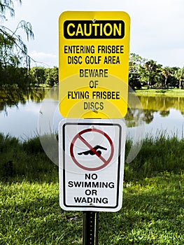 Disc Golf Caution Sign with No Swimming Sign on The Same Post