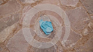 Discarded blue surgical mask lying on a textured stone pavement